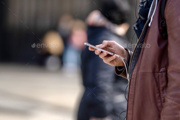Attractive adult successful fashion man in brown jacket using mobile phones on the city street