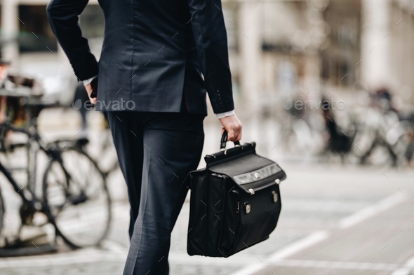 Businessman from behind with hand in pocket walking on city street to office with black briefcase