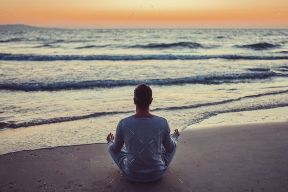 Candid authentic male millennial sitting in lotus pose on the ocean ...