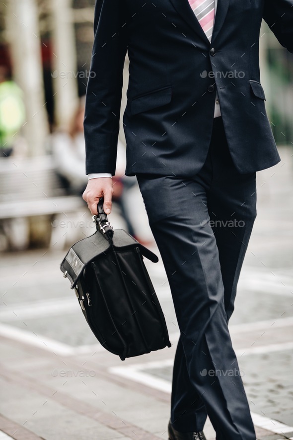Businessman at black fashion suit walking on city street to office with black bag
