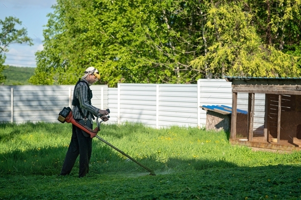 a young man mows the grass in his area with a garden trimmer
