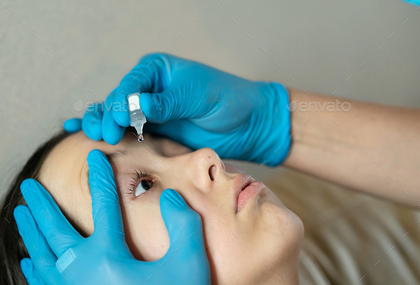 Testing new eye drops. hands in blue gloves open the girl’s eye and drip drops
