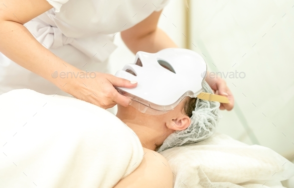 the cosmetologist puts on a led face mask. facial skin treatment with LED phototherapy