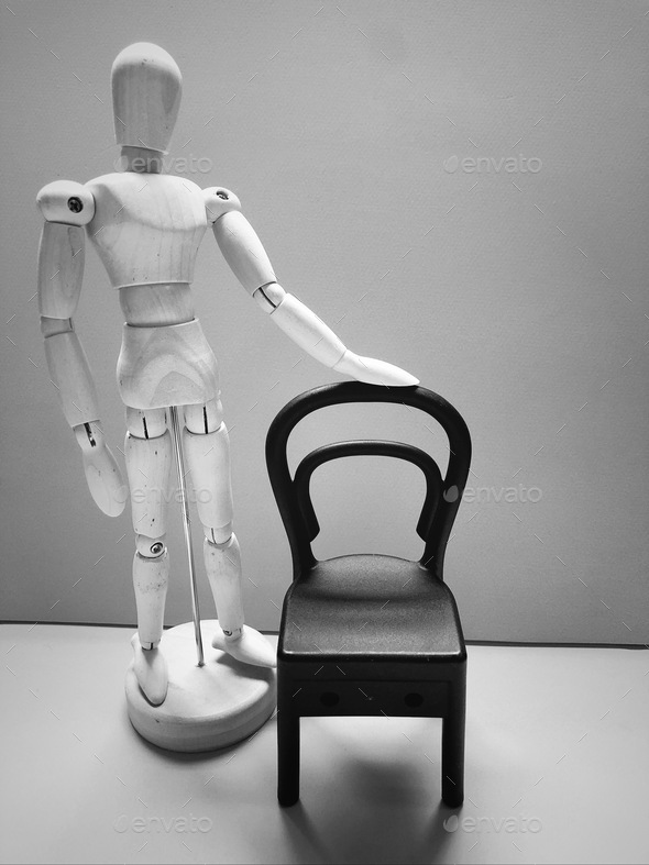 Have a seat. Artist mannequin (wooden dummy) posing with an empty chair. Black and white photo.