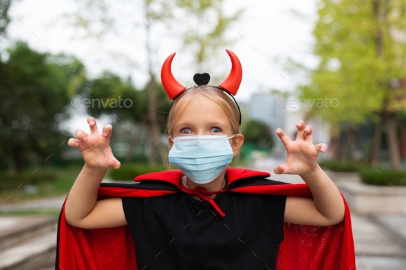 Portrait of cute Little Girl in costume of evil in park. Happy Halloween during coronavirus covid-19
