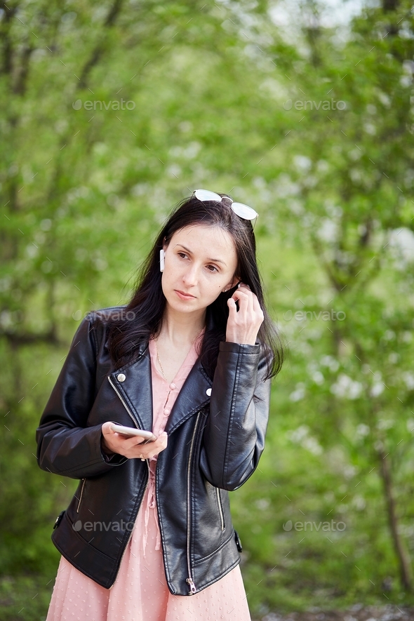Stylish girl listening to music by phone outside in the park. Spring walking, enjoying the moment