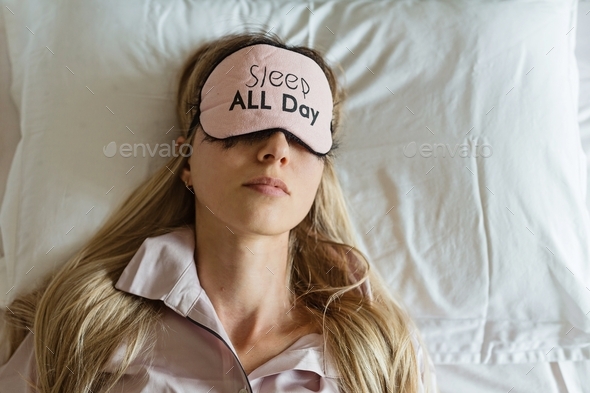 Young beautiful Caucasian woman with blonde hair sleeping in bed, wearing pajamas and blindfold