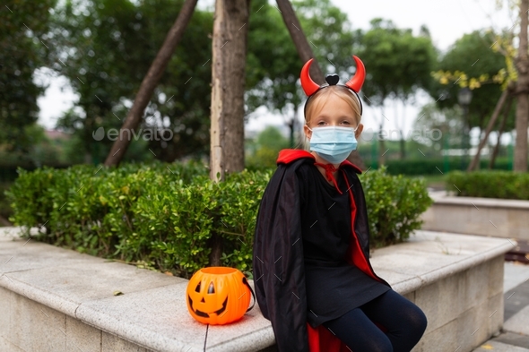 Portrait of cute Little Girl in costume of evil in park. Happy Halloween during coronavirus covid-19