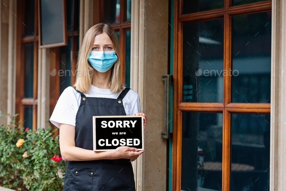 Restaurant owner wearing protective face mask and holding note sorry closed due to covid-19
