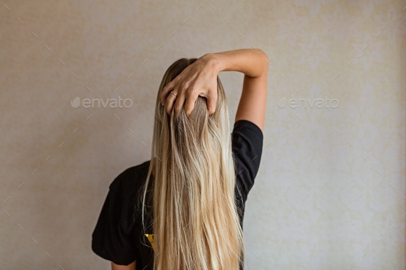 Young Caucasian woman with long blonde hair from behind on brown background