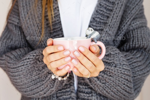 Woman holding hands cup of coffee or tea. Manicure in pastel colors, wearing cozy knitted cardigan