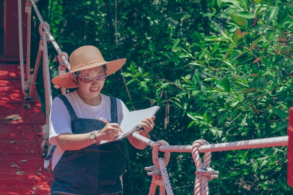 Portrait of female tourist taking notes on hanging bridge in mangrove forest at natural parkland