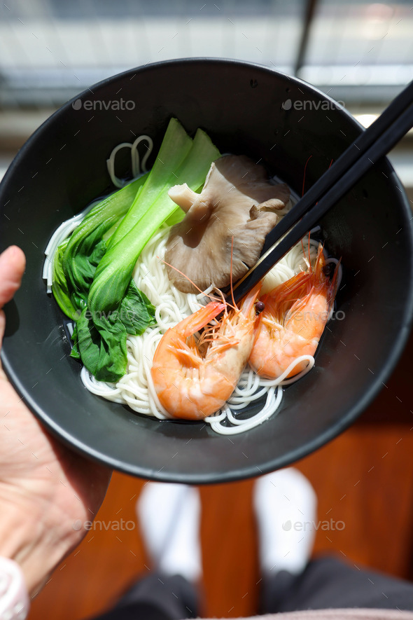 Woman holding hand black bowl with traditional Korean breakfast food ramen on kitchen at home