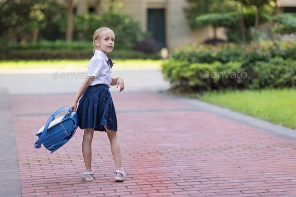 Schoolgirl back to school after vacations. Pupil in uniform and backpack early morning outdoor