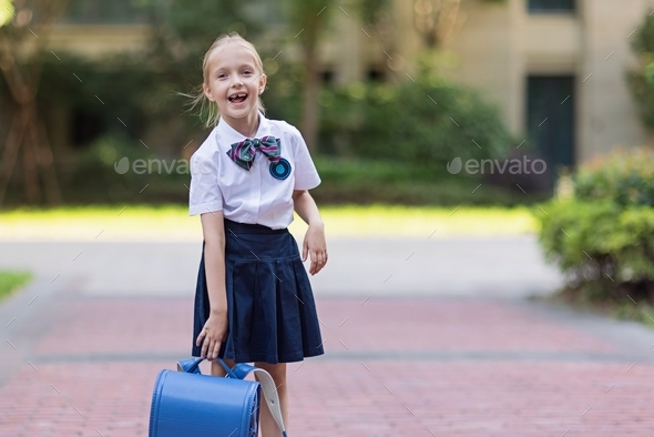 Schoolgirl back to school after vacations. Pupil in uniform and backpack early morning outdoor