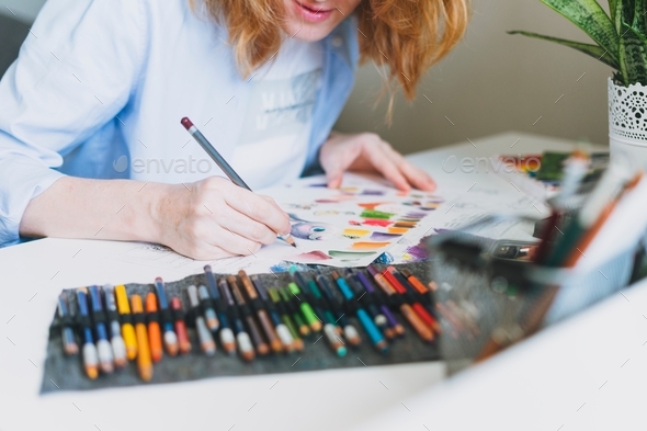 Young woman with red hair illustrator artist draws at desk at the home office