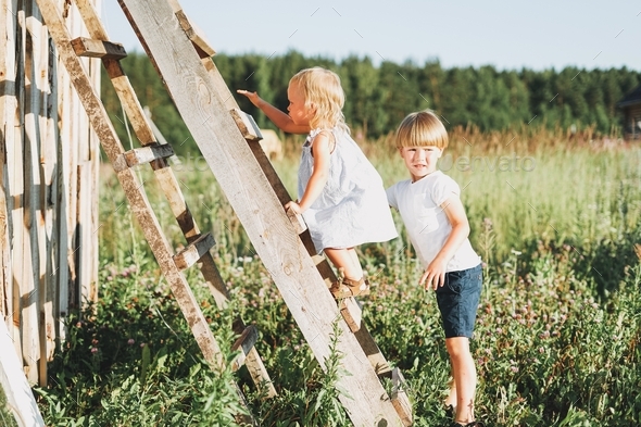 Cute siblings little girl and boy brother sister climbs up the ladder countryside cottagecor