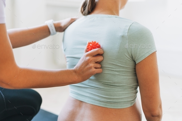 The trainer massages pregnant woman\'s back with spiked ball in bright studio