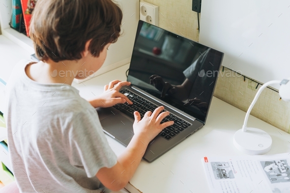 Tween boy do homework learn foreign language writing in pupil book with opened laptop at room home