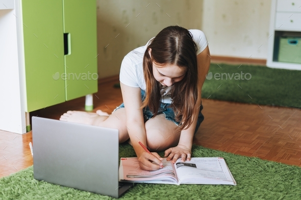 Attractive girl teenager do homework learn foreign language writing in pupil book with opened laptop