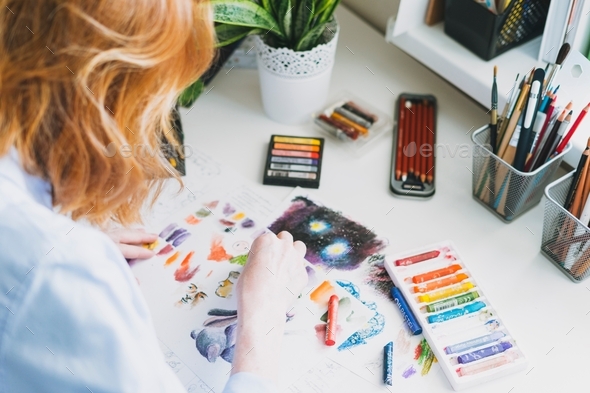 Young woman with red hair illustrator artist draws at desk at the home office