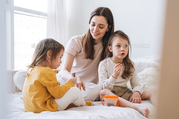 Young happy mother with two children girls eating on couch at home