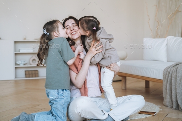 Young happy mother with two children girls kissing mom on couch at home