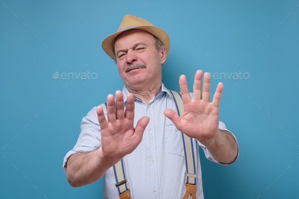 Attractive mature man in summer hat showing refusal gesture