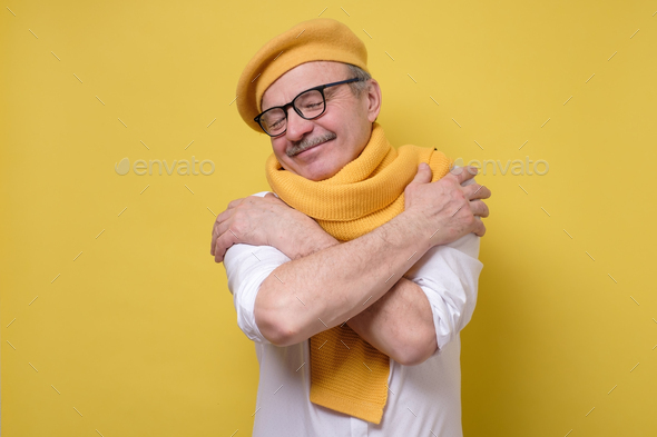 man in glasses and yellow hat and scarf hugs himself, has high self esteem