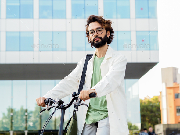 Young digital entrepreneur man with a bike in a financial district looking at camera