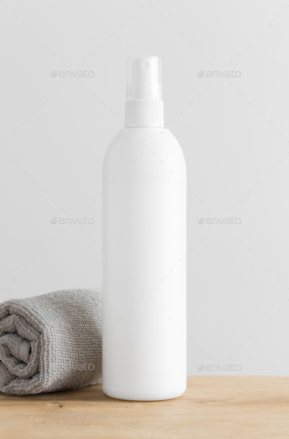 White cosmetic spray bottle mockup with a towel on a wooden table.