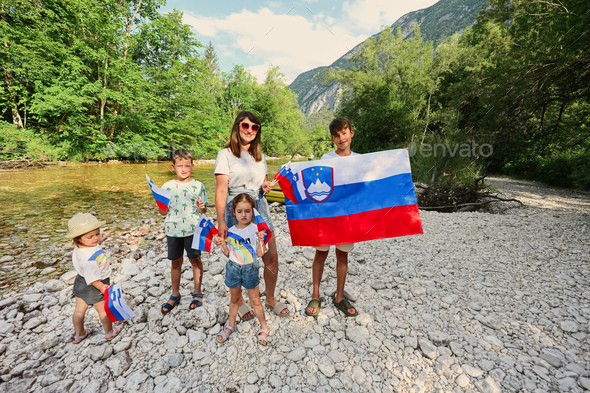 Mother with kids hold slovenian flags in rocky shore of a calm river