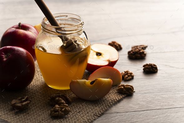 Mason jar with honey honey dipper red apples and walnuts on kitchen table - Stock Photo - Images