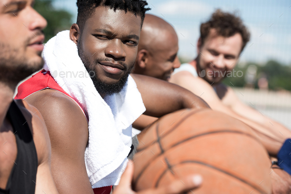 side view of multicultural basketball team resting after game on court
