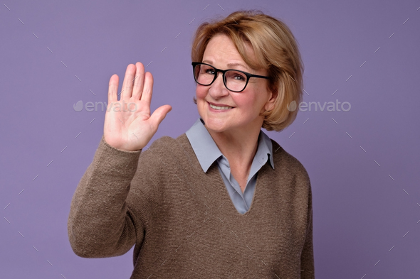 Senior caucasian woman smiling happily, saying Hello, Hi or Bye, waving hand