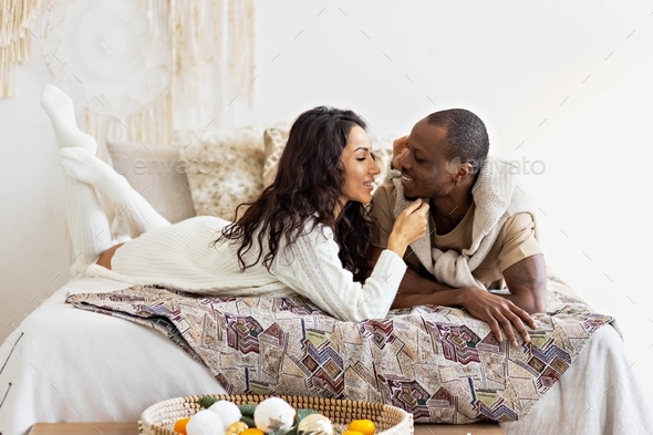 A couple in love - a black man and a mulatto woman on a bed in a bright ...