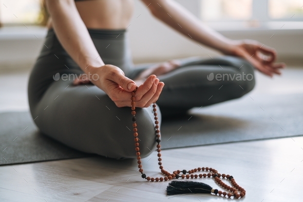 Young fit woman practice yoga doing asana lotus position meditation with beads in light yoga studio
