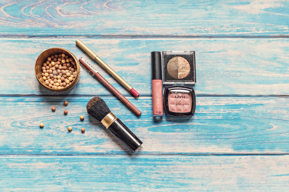 On a blue wooden background, blush in balls, brush, eye and lip pencils, eye shadow, lip gloss