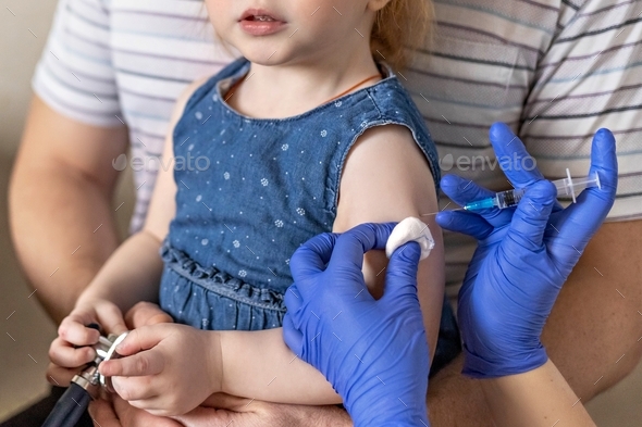 A little girl in the doctor\'s office at the clinic is being vaccinated against the coronavirus.