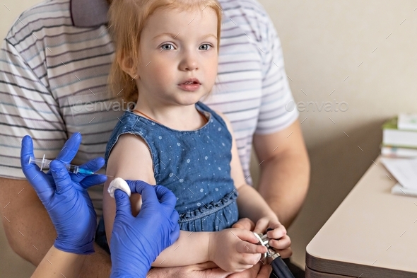 A little girl in the doctor\'s office at the clinic is being vaccinated against the coronavirus.