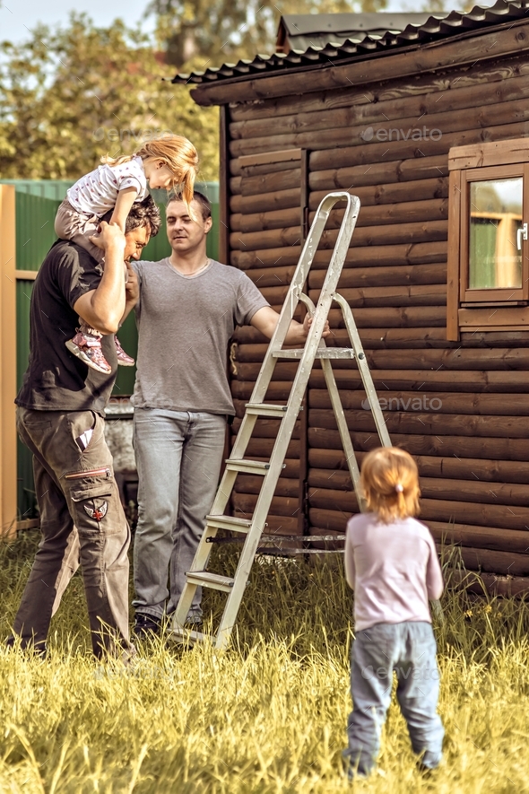 Two dads together with their daughters are repairing a shed in the backyard. Family on a weekend in