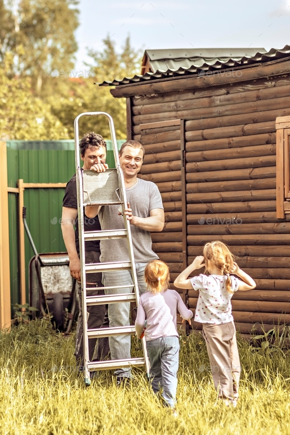 Two dads together with their daughters are repairing a shed in the backyard. Family on a weekend in