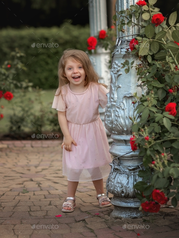 little caucasian cheerful girl in a field of roses with roses in her hands
