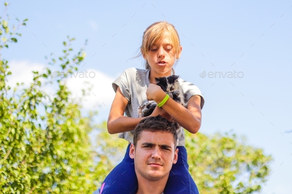 Portrait of happy girl on man shoulders, piggyback. Girl holding cat, kitten