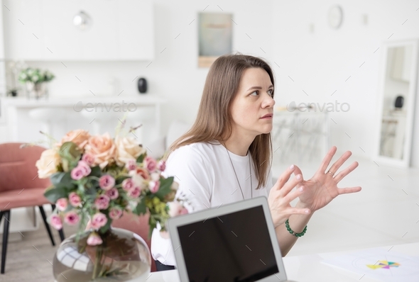 a young female coach works in a home office in a light interior with a laptop and flowers on the tab