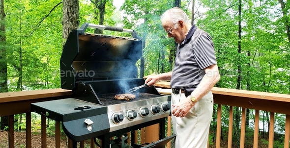 Senior dad is young at heart cooking steaks on the gas grill on outdoor living space among the trees