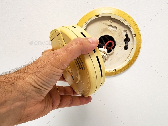 Man hand opening up built in smoke alarm to change battery to shut the beep up.