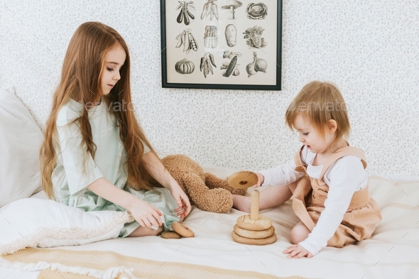 two red haired siblings sisters are sitting on bed in cosy country house on summer vacation and play