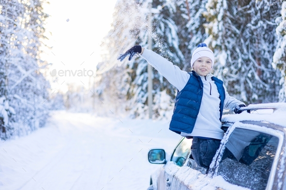 teenage boy in white sweater, vest and white knitted hat in car window in snowy forest having fun, c