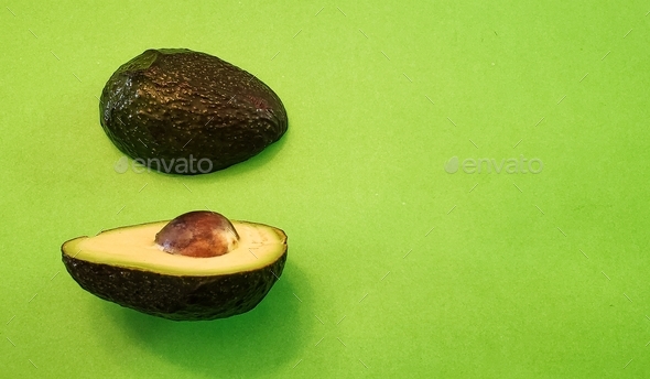 A ripe ready to eat sliced in half Avocado on a green background.